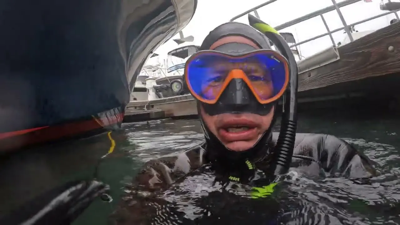 A still from Daily Divers: a diver in a mask and snorkel in the water beside the bow of a boat.