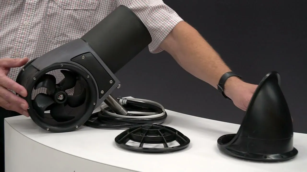 A still from Imtra: hands on an SX external stern thruster on a white table, its nose cone and grilles beside it.