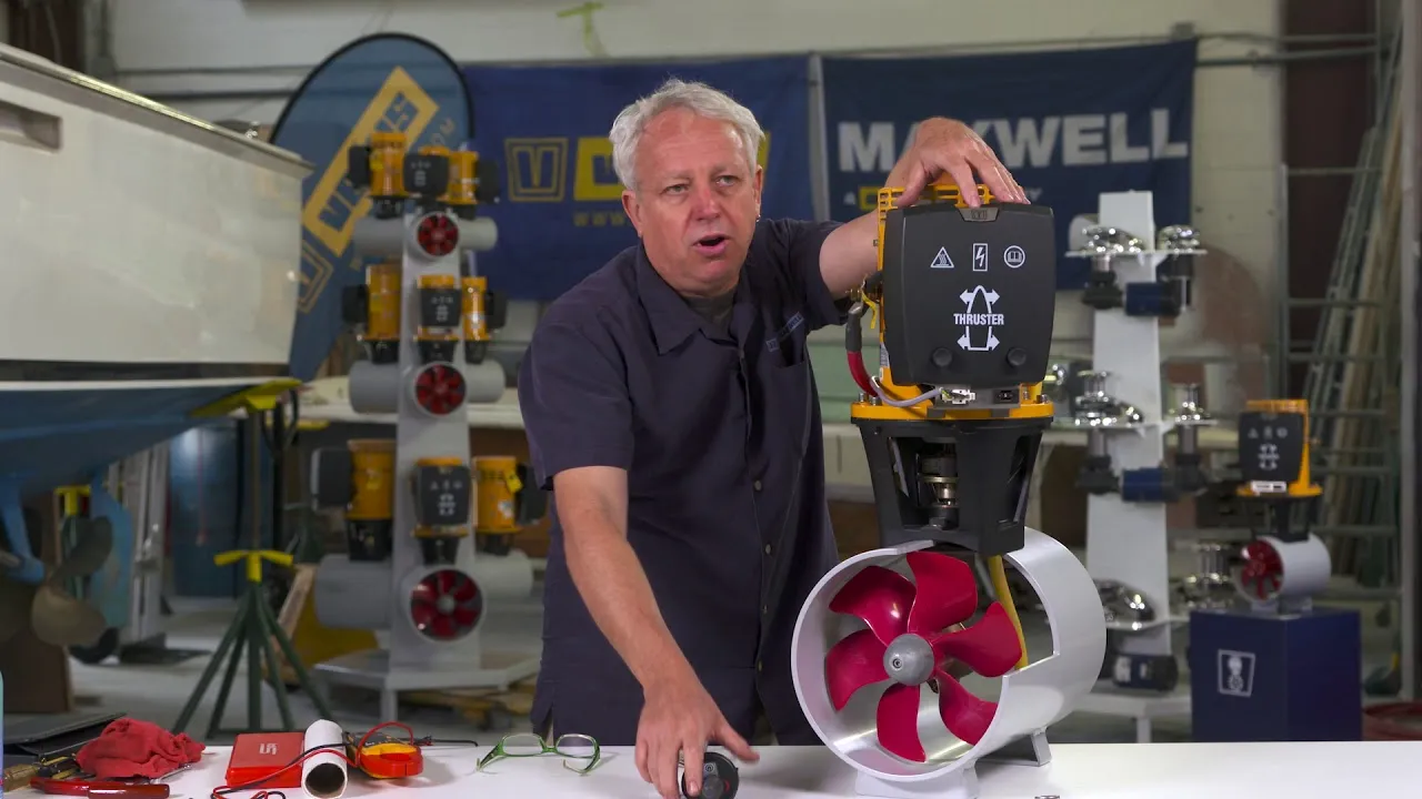 A still from VETUS's maintenance video: a presenter in a workshop with his hand on a tunnel thruster's motor, its red propeller in a cutaway tunnel below.